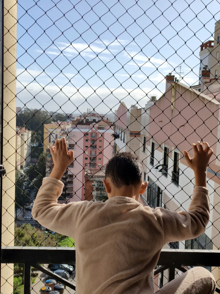 Criança protegida por rede de proteção em varanda de apartamento.